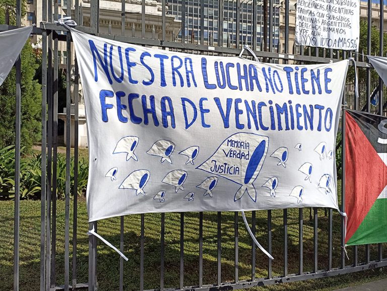 An einem Gitterzaun hängt ein Stofftransparent mit der Aufschrift: "Nuestra Lucha no tiene fecha de vencimiento"